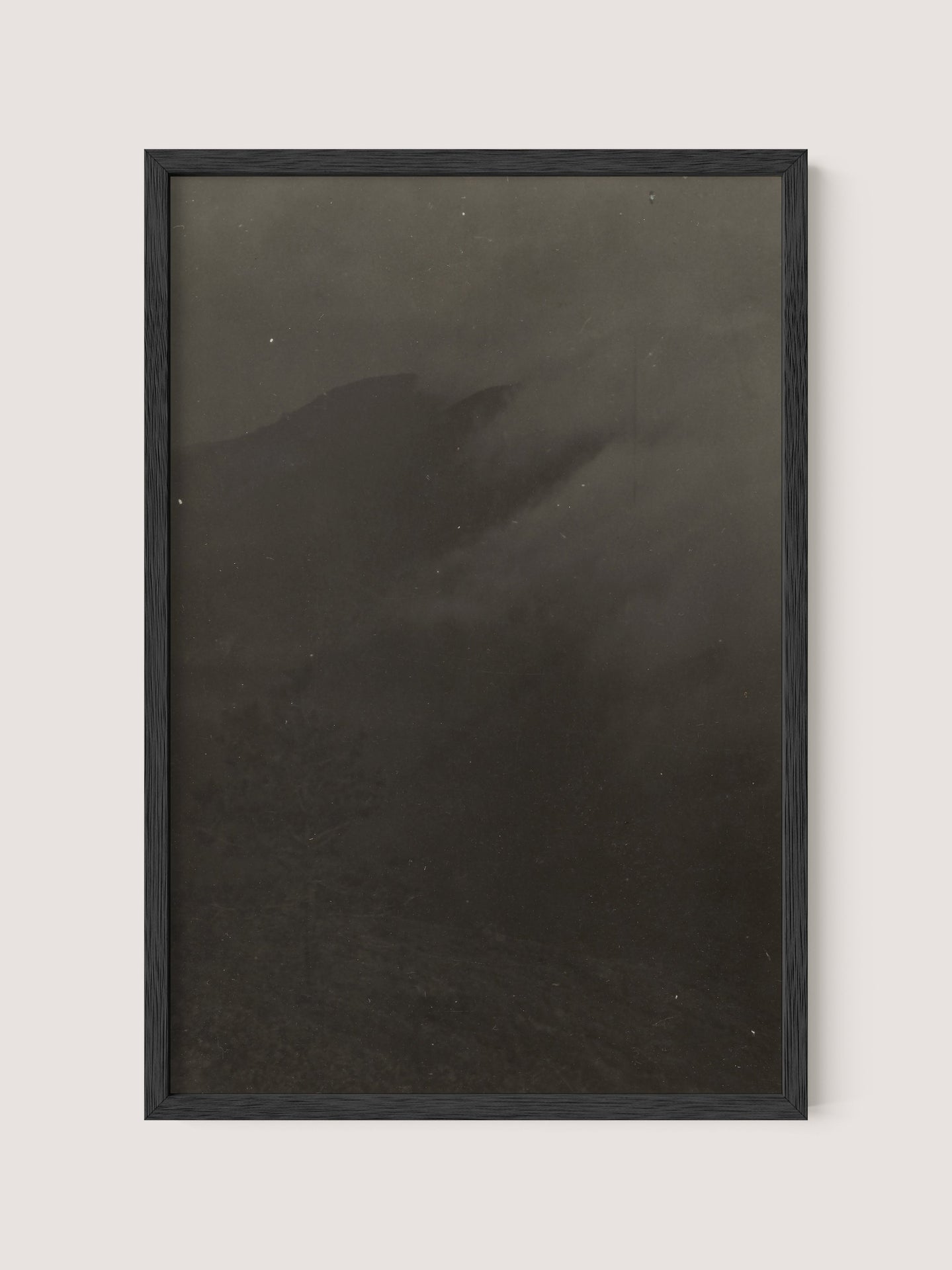 Mountain Landscape, framed in elegant Black Oak, presents a dark and moody photograph of an obscured terrain with faint outlines of mountains and misty clouds. This grainy masterpiece, reminiscent of 19th Century American photography, evokes mystery and depth akin to the timeless black-and-white prints by Louis Fleckenstein.