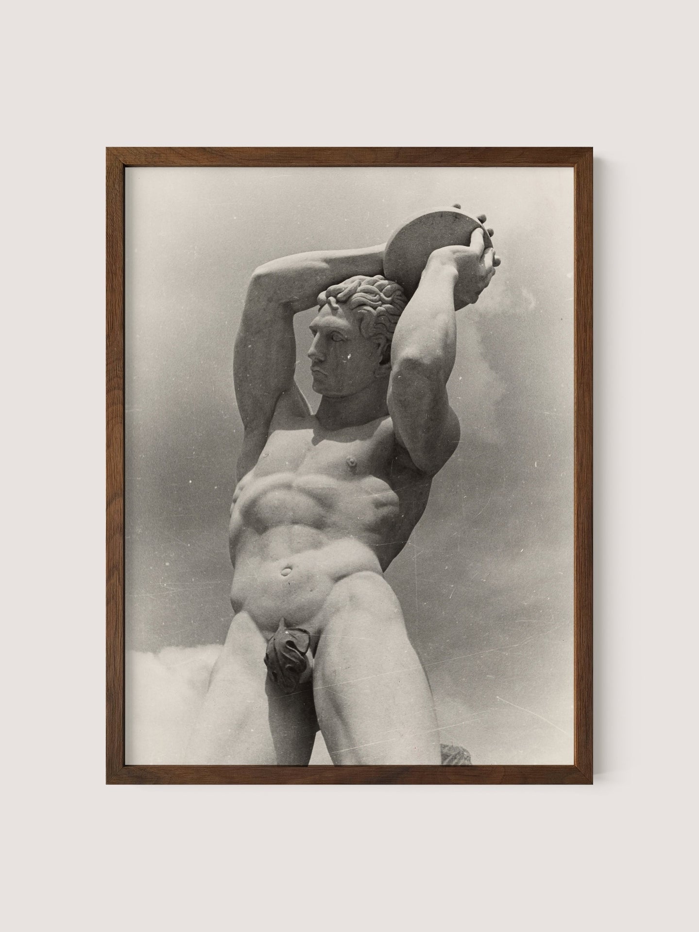 A photograph by Paul Wolff captures The Discus Thrower, a classical male nude statue with muscular form, lifting a circular object above its head with both hands. The framed image in Walnut Oak is set against a light background.