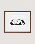 The "Samantha Michell III" framed minimalist art print features an original ink drawing of a reclining nude figure against a dark, irregular background. The print is elegantly displayed within a wooden frame made from walnut premium oak and centered within a white matte border, hung on a light-colored wall. This exceptional piece is part of an exclusive edition of 10.