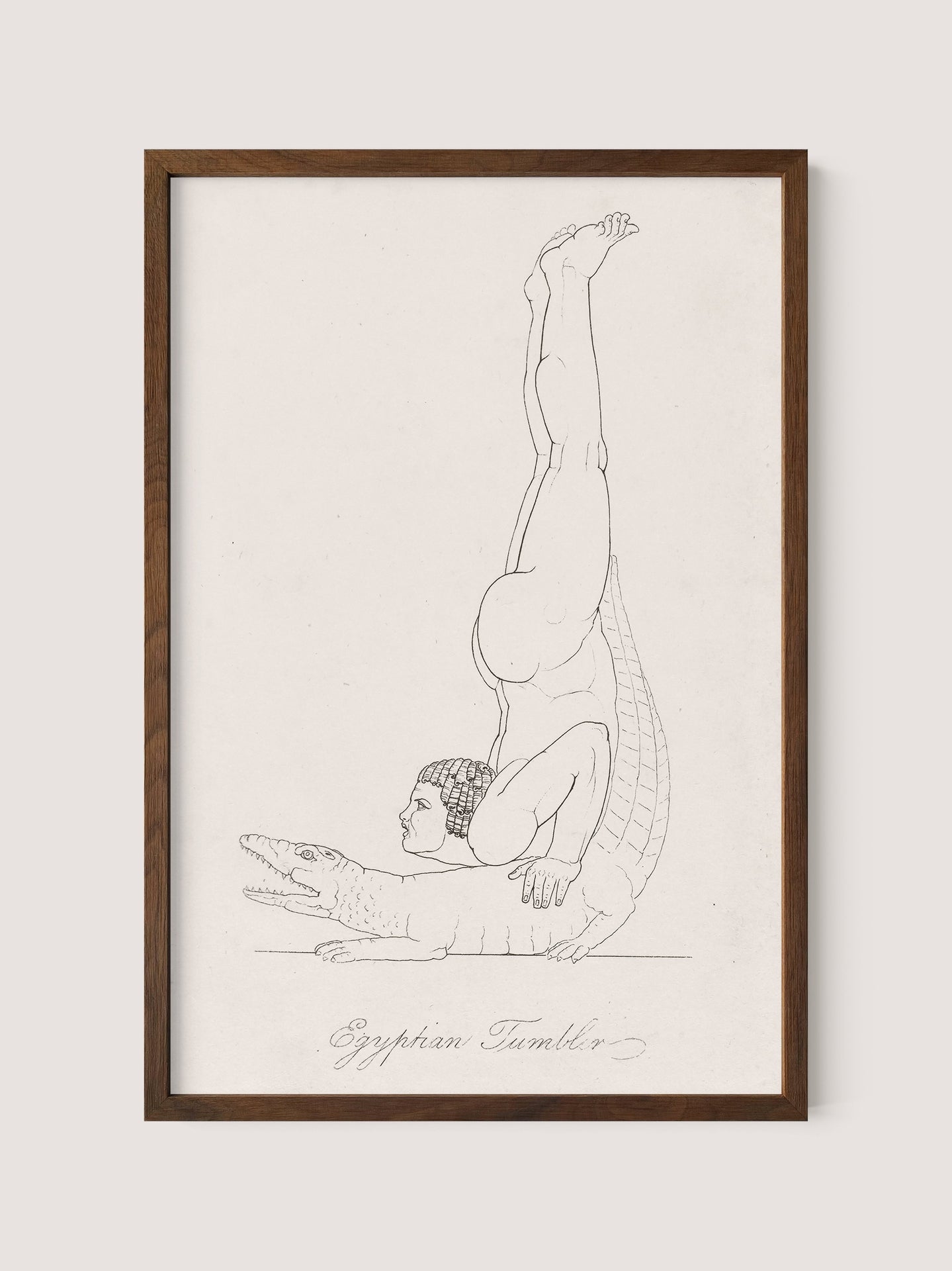 The &quot;Egyptian Tumbler&quot; framed artwork, in a Walnut Oak finish, depicts a man in Roman costume balanced upside down on a crocodile&#39;s back. The man performs a headstand with his legs extended vertically, while the crocodile lies horizontally, facing forward. The artwork features minimalist design with fine lines.