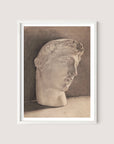 Introducing "Study of a Plaster Head," a framed monochrome sketch featuring the head of a classical sculpture of a young man with curly hair in a slightly downward-facing profile view. Set against a neutral background and framed in sleek White Oak, this neoclassical piece exudes minimalist elegance, capturing timeless beauty with simplicity and grace.