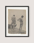 A framed vintage photograph titled "Beach Walk," reminiscent of Thomas Eakins' work, depicts two nude individuals standing on a beach. They face away from the camera, gazing toward the water with a small boat to their left. The image's sepia tone enhances its aged appearance, reflecting a timeless creative process in photography. The frame itself is finished in Black Oak, adding an elegant touch to this evocative piece of art.