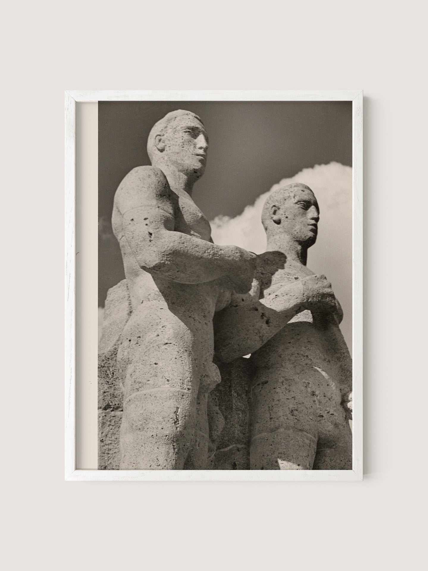 A black and white photograph titled "Olympic Men, Berlin" in a white oak frame depicts two stone statues positioned side by side. The statues, reminiscent of the Berlin Olympic statues from the 1936 Olympic Games, have a weathered, ancient appearance with muscular forms and serious expressions. A cloudy sky serves as the backdrop.