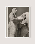 A black and white photograph titled "Olympic Men, Berlin" in a white oak frame depicts two stone statues positioned side by side. The statues, reminiscent of the Berlin Olympic statues from the 1936 Olympic Games, have a weathered, ancient appearance with muscular forms and serious expressions. A cloudy sky serves as the backdrop.