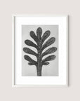 The Yarrow Leaf framed artwork features a black and gray abstract depiction of a tree with multiple branches resembling thick, rounded leaves, displayed against a light gray background. This painterly print captures botanical beauty in a simple White Oak frame.