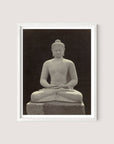 A framed photograph of a serene white oak Buddha Statue in a meditative seated posture against a dark background. The statue, reminiscent of those found in a Buddhist sanctuary, has a calm expression, closed eyes, and its hands resting on its lap in a traditional meditation pose.