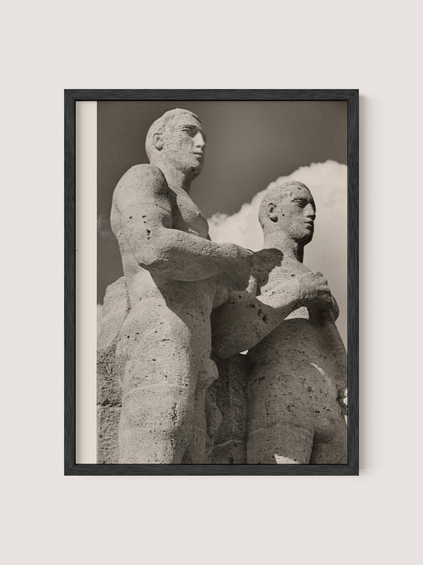 The framed black and white photo titled "Olympic Men, Berlin" encapsulates the essence of Paul Wolff's photography, featuring two stone statues often recognized as Berlin Olympic statues. The sculptures depict two muscular male figures, one slightly ahead of the other, gazing forward against a sky with a few clouds and are beautifully presented in a Black Oak frame.