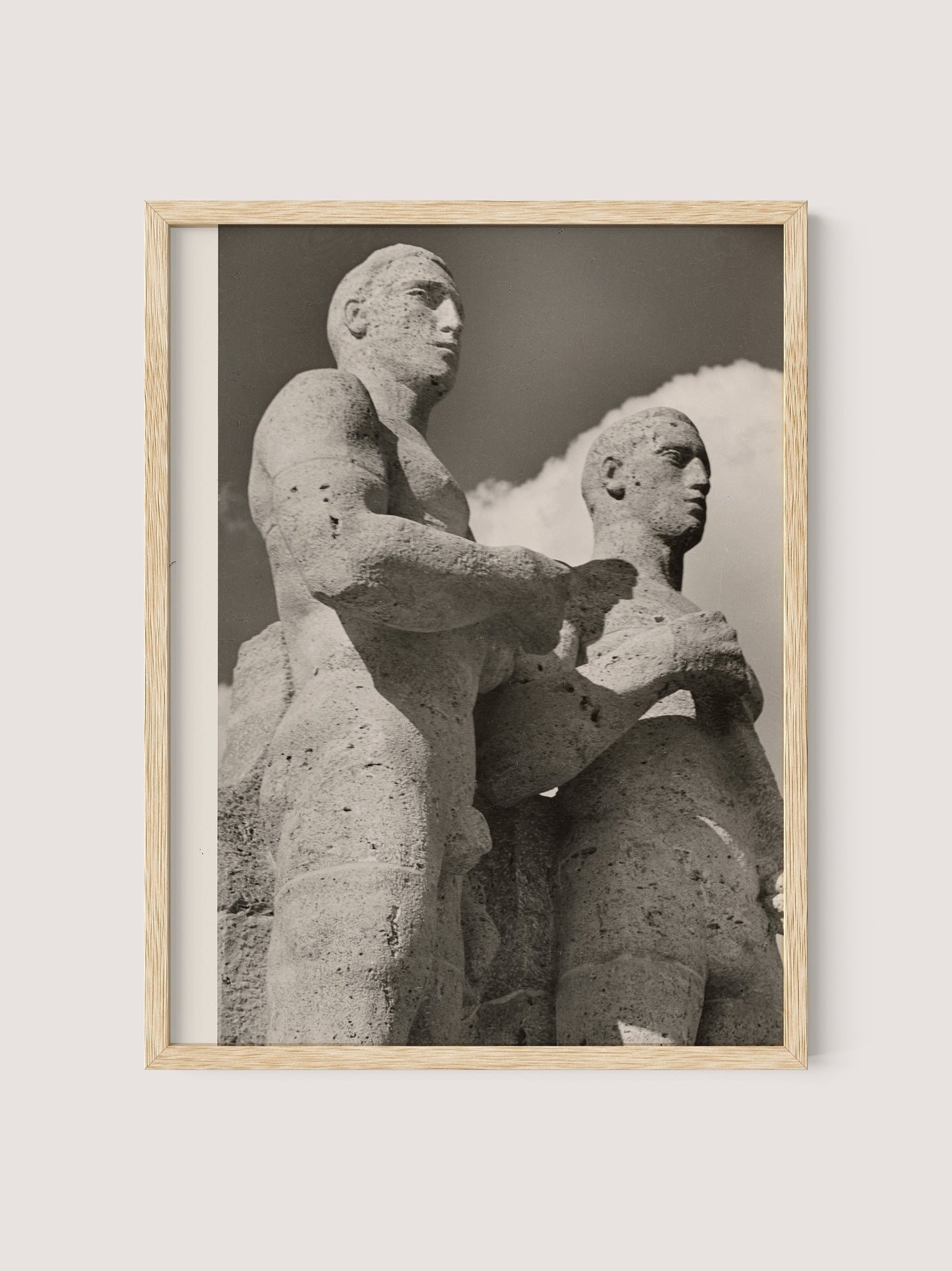 Framed black and white photograph titled "Olympic Men, Berlin," depicting two large Berlin Olympic statues standing close together. The statues are weathered and detailed against a backdrop of a partly cloudy sky. Captured by Paul Wolff during the 1936 Olympic Games, the frame is crafted from natural oak with a simple finish.