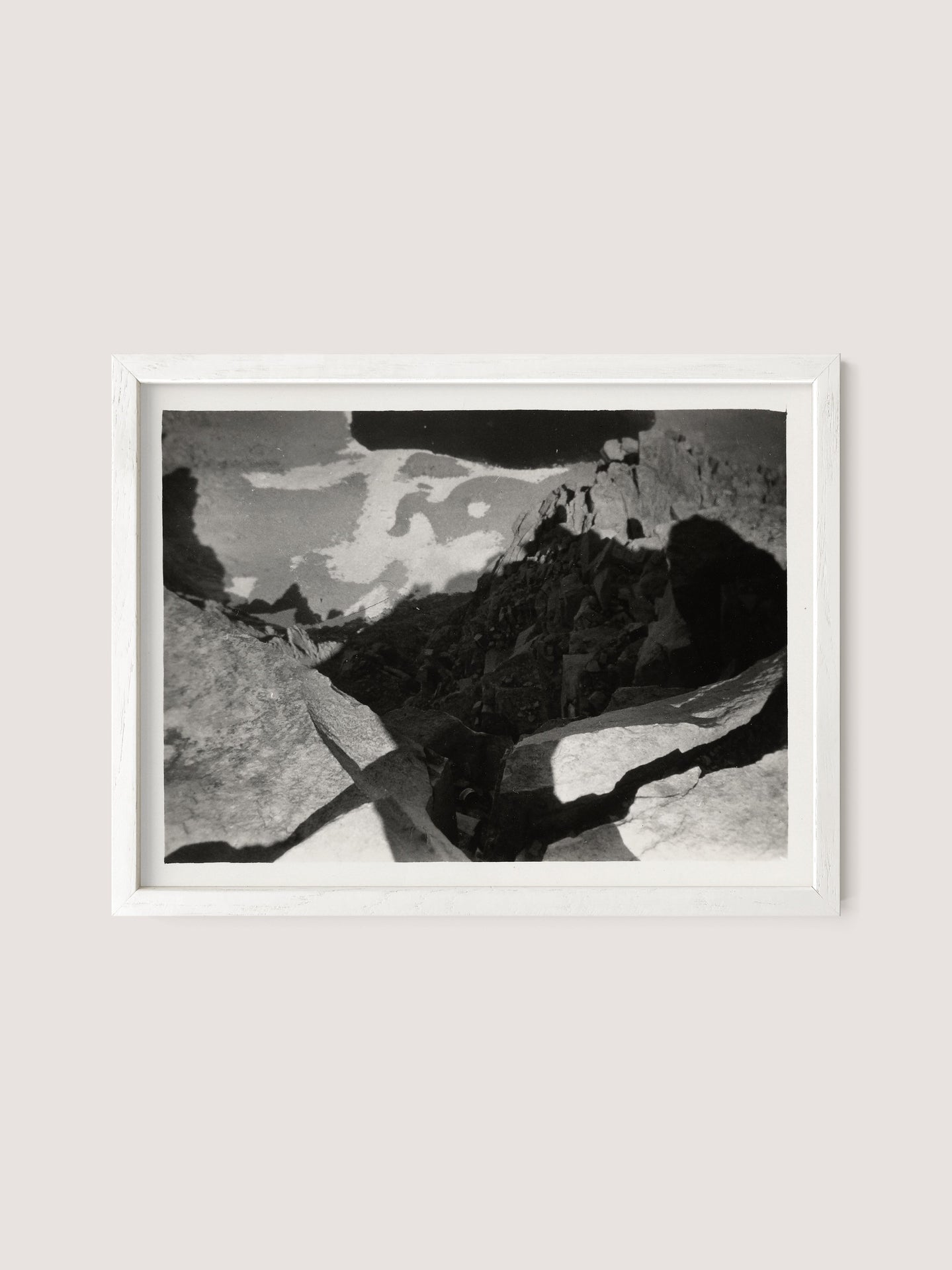 White oak-framed black and white photograph featuring a landscape with rocky terrain and shadows, capturing the dramatic interplay of light and dark areas. This photo titled "Looking Down From Mt. Whitney" by Louis Fleckenstein boasts a textured, abstract quality that enhances its captivating contrast.