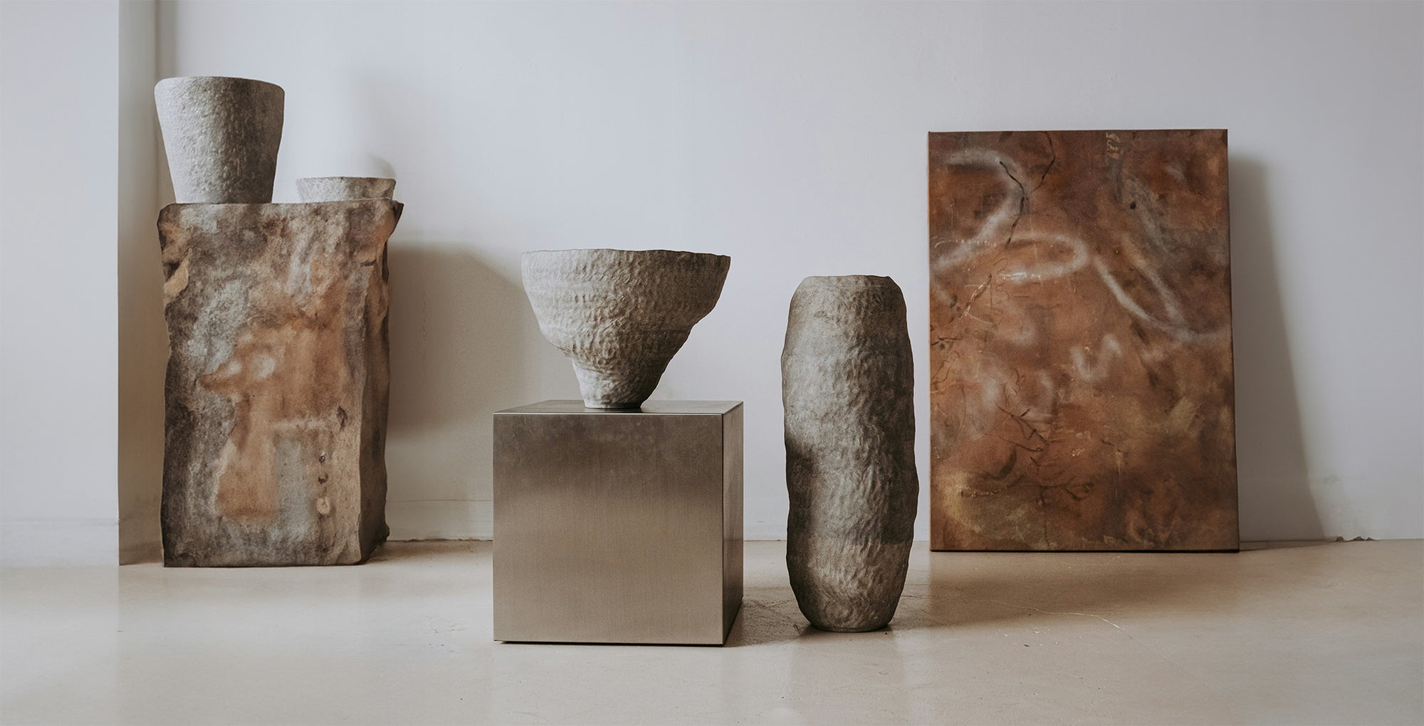 A small handful of hand-formed ceramic and maché vases on stone and metallic pedestals. 