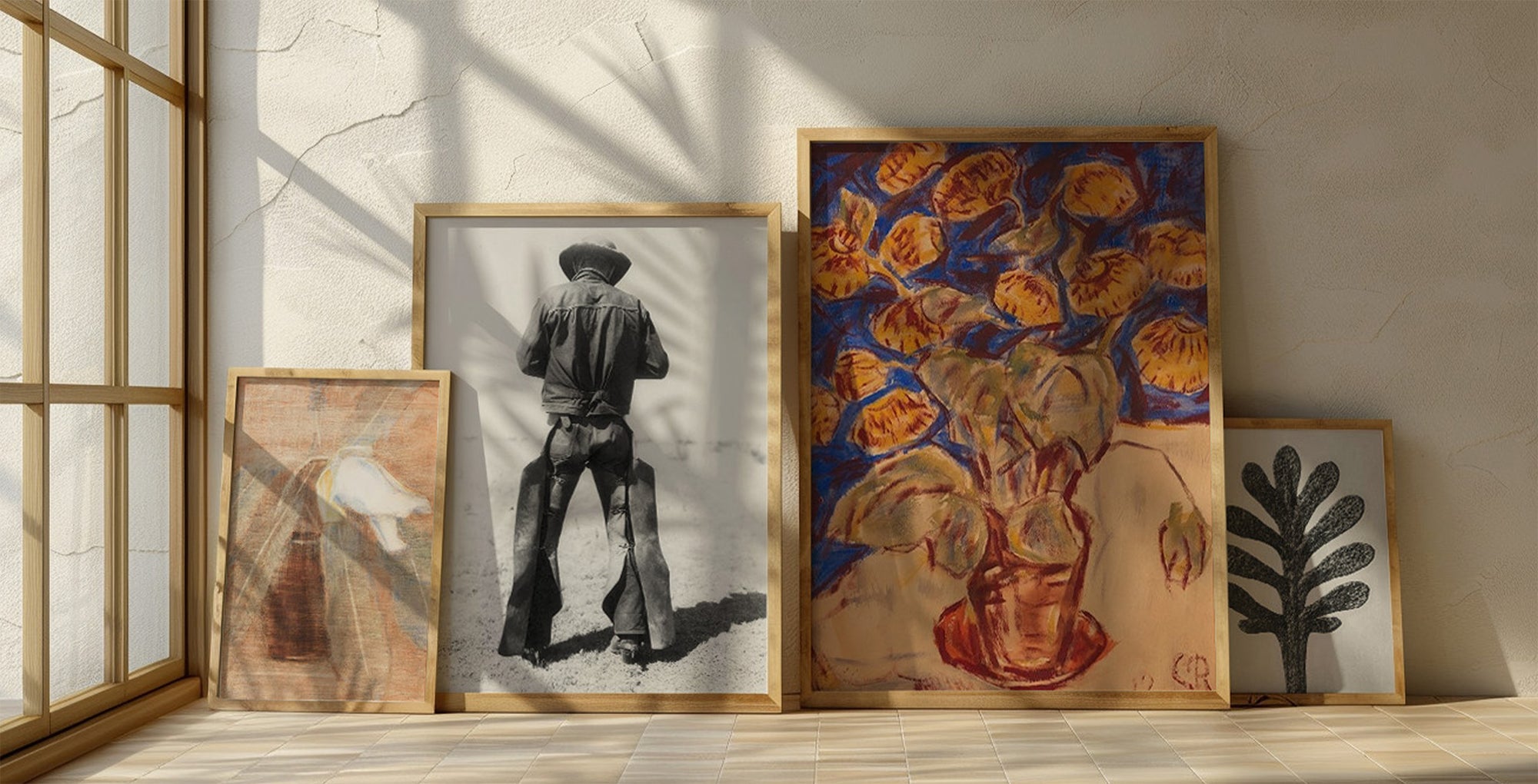 Collection of prints in blond-wood frames sitting on the floor with light coming in from the left side.