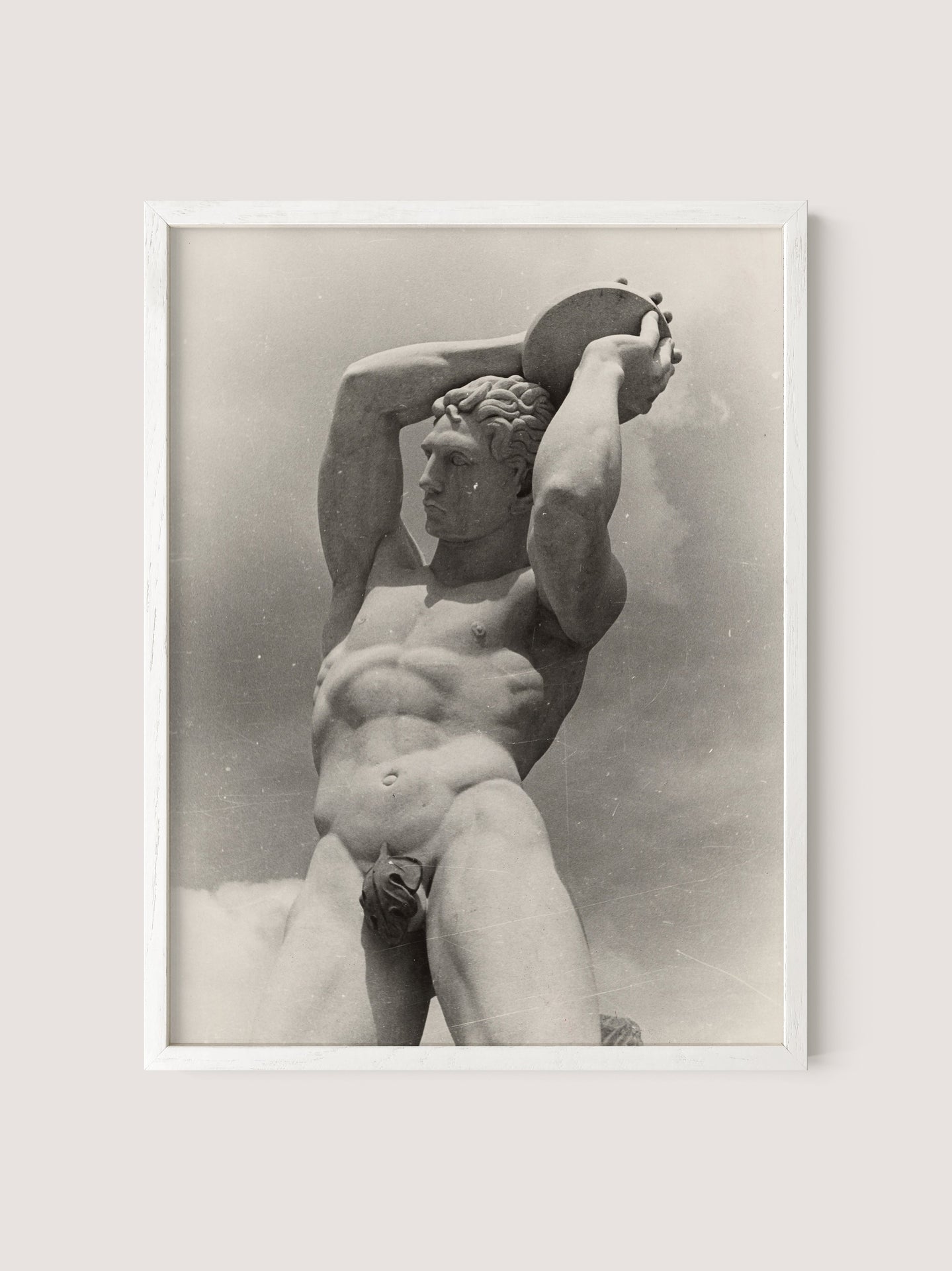 Black and white photograph of The Discus Thrower, a classical-style statue of a nude male figure holding a round object above his head. The statue appears muscular with detailed anatomical features. This Paul Wolff photo is framed in white oak and set against a pale background.