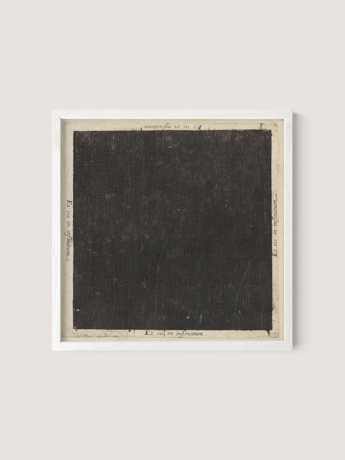 A framed artwork reminiscent of Flood's seminal piece, called "Cosmic Square," features a densely textured black square at the center, bordered by cream-colored margins that contain faint handwritten inscriptions. The frame is simple and white oak, contrasting subtly with the dark, almost abstract central area.