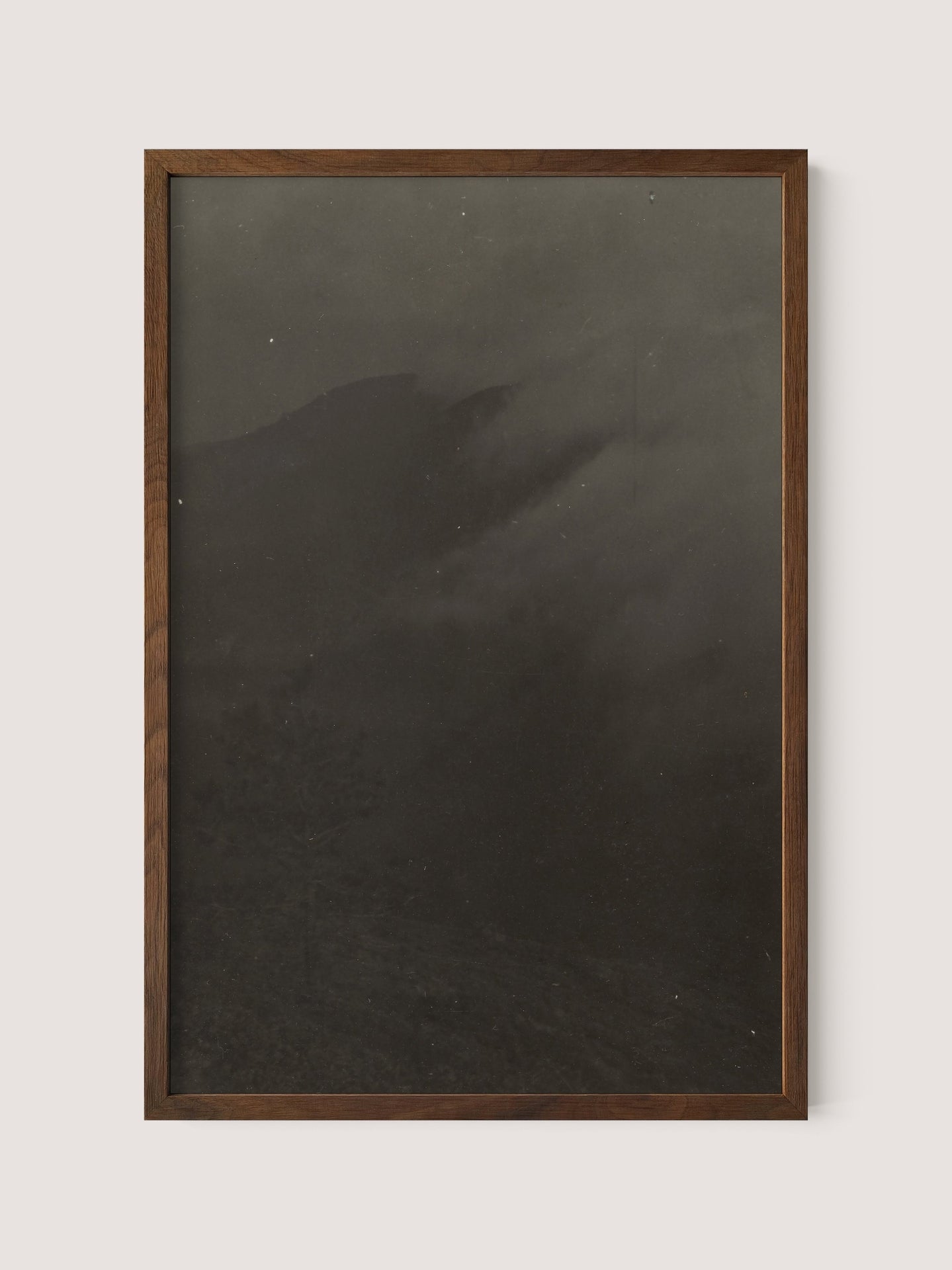 A wooden-framed picture named &quot;Mountain Landscape&quot; with a dark, indistinct image. The scene appears to depict a misty landscape, reminiscent of a black and white print by 19th Century American photographer Louis Fleckenstein. Its Walnut Oak frame complements the shadows that hint at hills or mountains shrouded in fog, creating an atmospheric, moody feel.