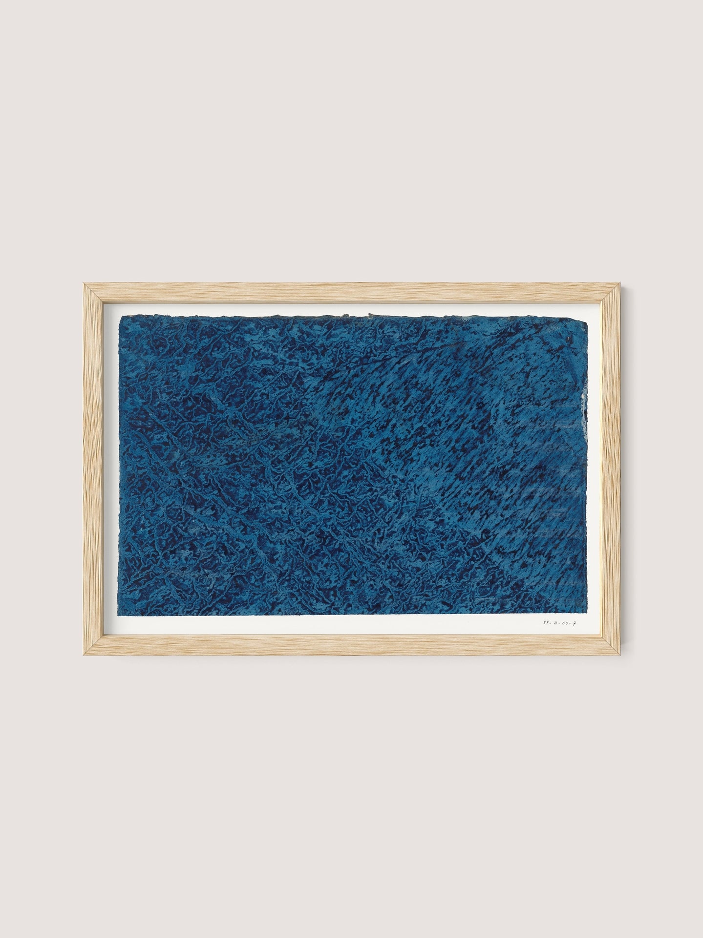 A framed artwork features a rectangular piece with rich, textured blue patterns on a white background. The natural oak frame complements the bold hues of the Marbled Blue print, creating a striking visual contrast. The piece, exuding a timeless allure, is signed and dated in the bottom right corner.