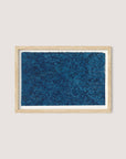 A framed artwork features a rectangular piece with rich, textured blue patterns on a white background. The natural oak frame complements the bold hues of the Marbled Blue print, creating a striking visual contrast. The piece, exuding a timeless allure, is signed and dated in the bottom right corner.