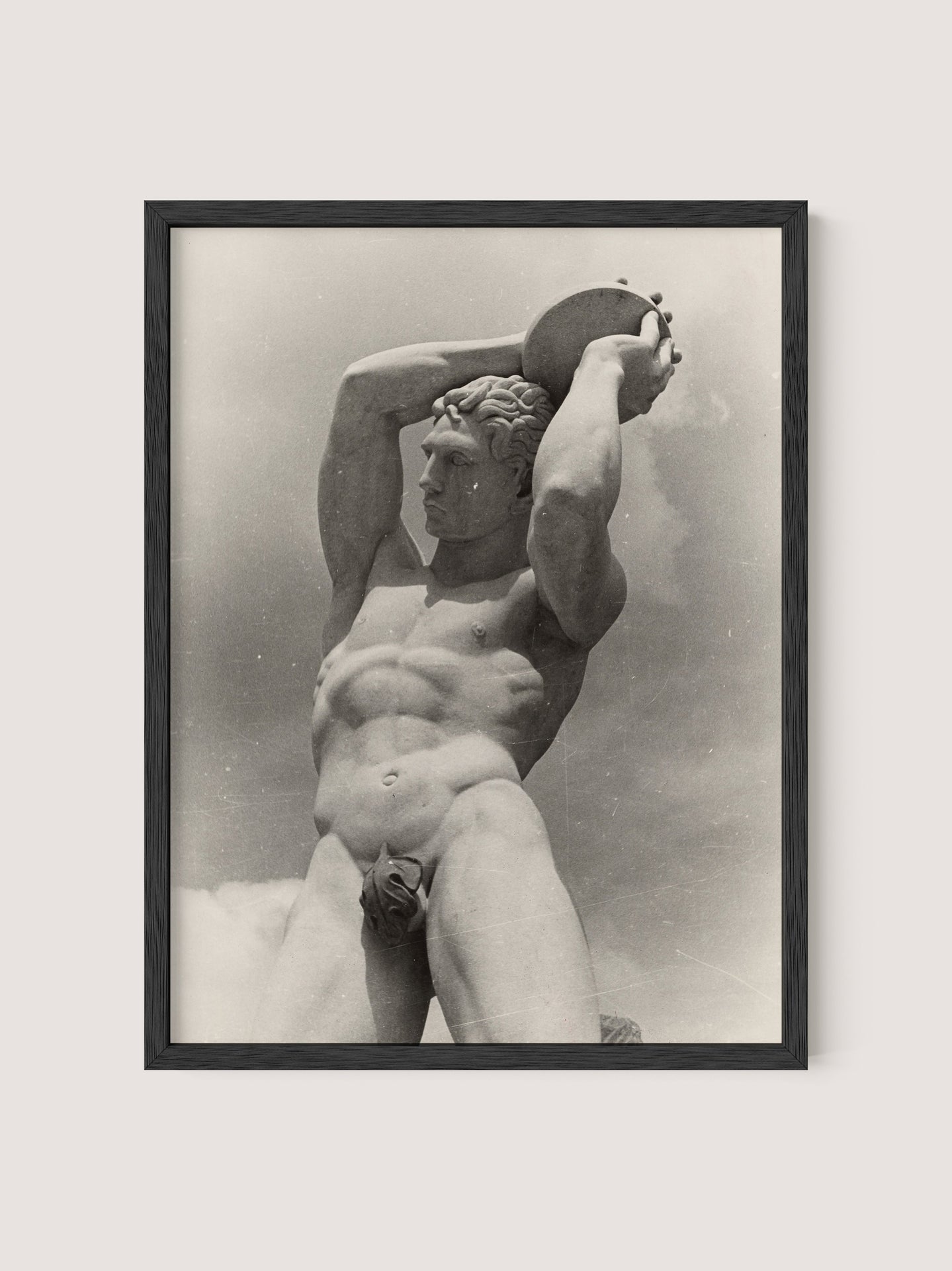 A black and white photograph of The Discus Thrower, a nude male statue holding a disc above his head with both hands. The statue appears muscular and detailed, with a focus on strong posture and serene expression. Paul Wolff's striking image is elegantly framed in Black Oak.