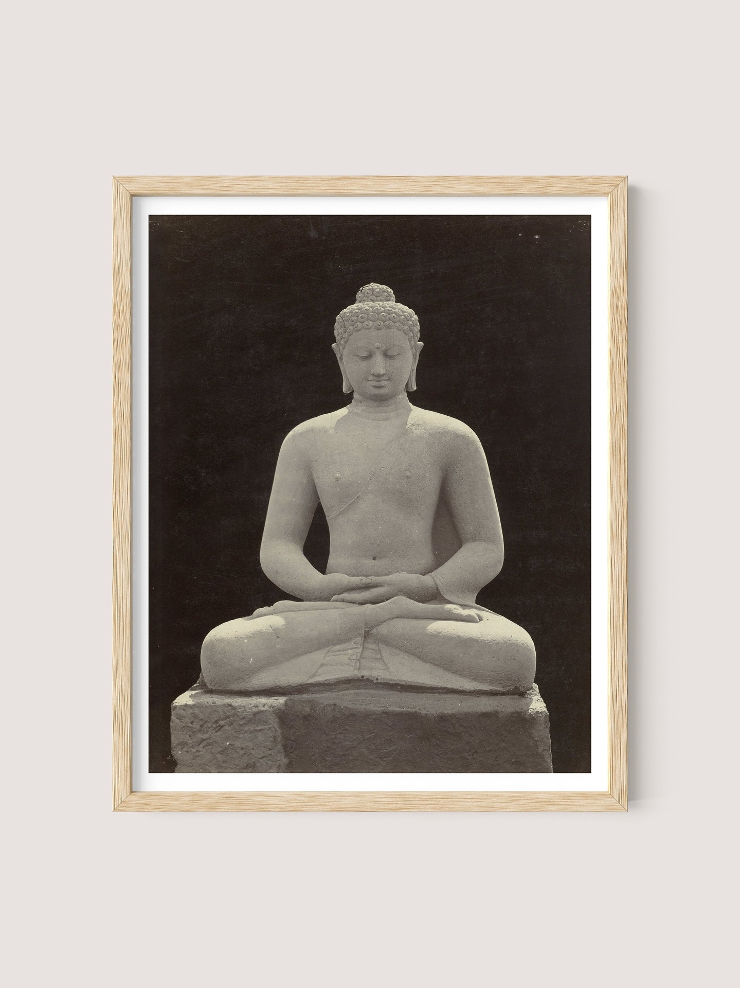 A Buddha Statue, encased in a light wooden frame of natural oak, depicts a serene, seated meditative pose with legs crossed and hands resting in its lap. Resembling the ancient figures of Borobudur, the stone statue sits against a dark background.