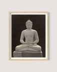 A Buddha Statue, encased in a light wooden frame of natural oak, depicts a serene, seated meditative pose with legs crossed and hands resting in its lap. Resembling the ancient figures of Borobudur, the stone statue sits against a dark background.