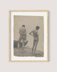 A framed photograph titled "Beach Walk," encased in natural oak, captures two nude figures standing on a rocky shoreline, reminiscent of Thomas Eakins' creative process. The figures, with their backs to the camera, appear contemplative; one stands upright while the other leans slightly with a hand resting on their lower back. A boat is visible to the left.