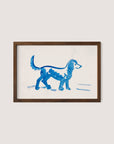 A framed artwork by Peter Weisz Kubínčan, titled "Great Dane," depicts a simplistic painting of a blue Great Dane walking, rendered with broad, fluid brushstrokes on a white background. The walnut oak wooden frame contrasts with the minimalistic and playful style of the painting, making it perfect for blue-toned decor.